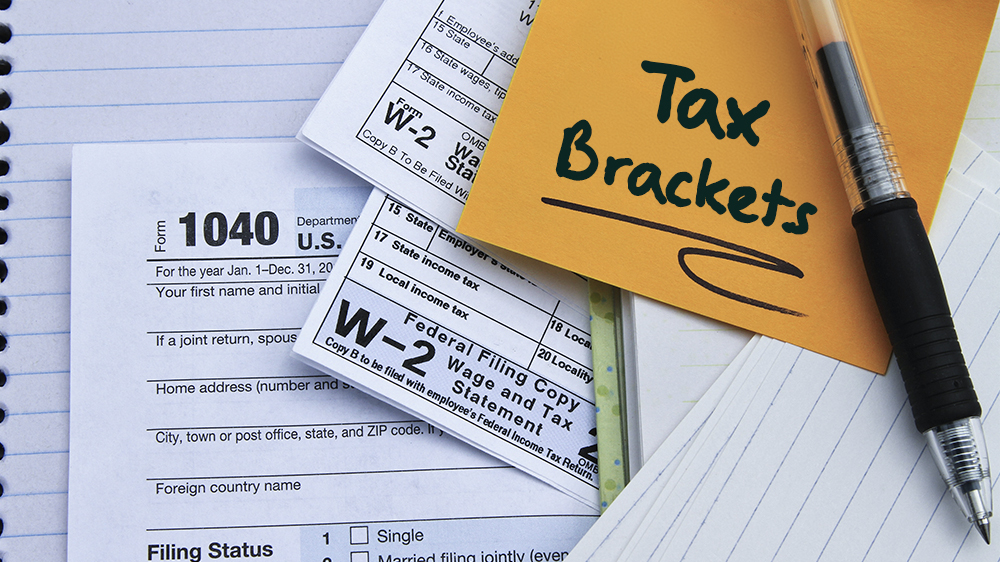 w-2 forms on a desk with a sticky note reading "Tax Brackets"