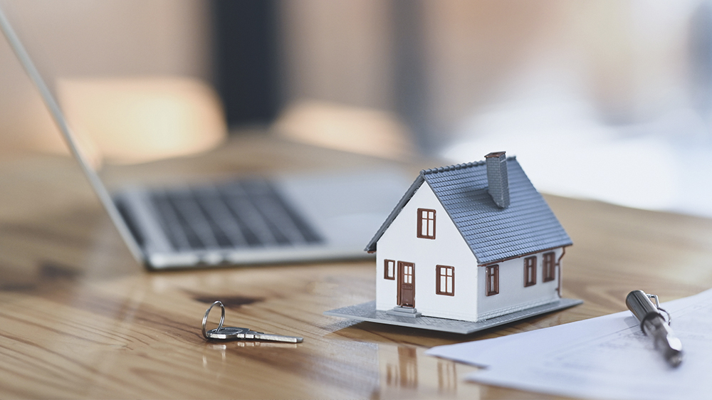 A small house figurine on a desk next to a laptop