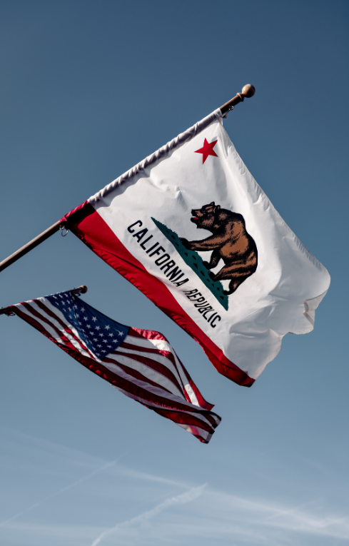 The california state flag and the united states flag flying against a clear blue sky