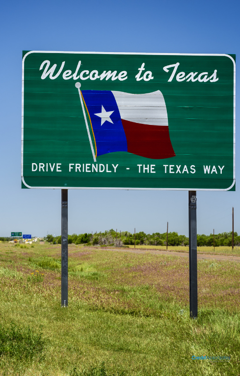 A welcome to texas highway sign with the state flag, under a clear blue sky